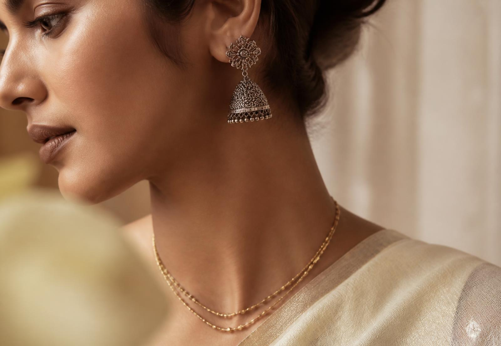 Model wearing oxidised silver jhumka earrings and a fine gold layering necklace